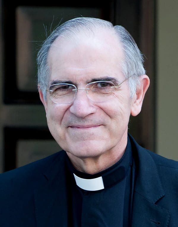 Sacerdote mayor con gafas y alzacuellos, mirando a cámara con expresión serena.