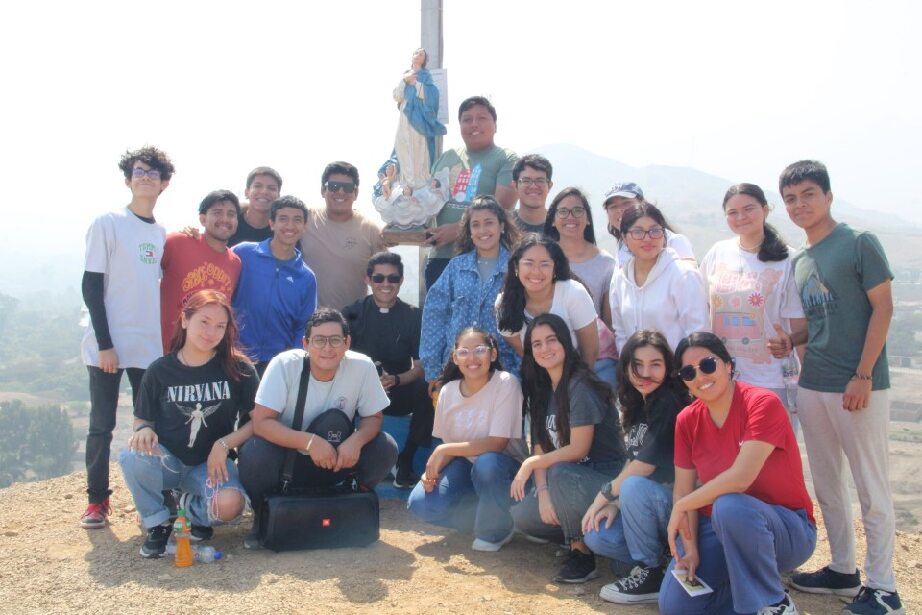 A group of young people during a Marian pilgrimage pose happily on the top of a mountain. 