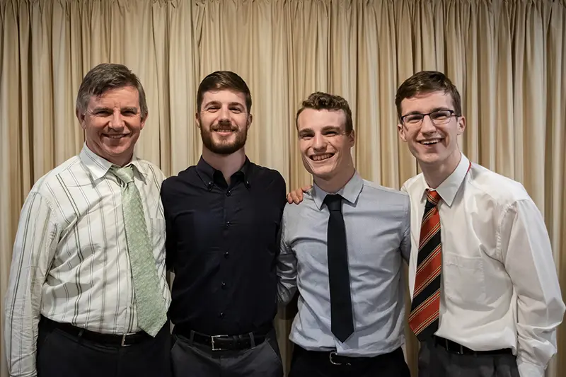 Samuel, seminarista neozelandés, sonríe junto a su padre y sus dos hermanos, todos vestidos de manera formal.