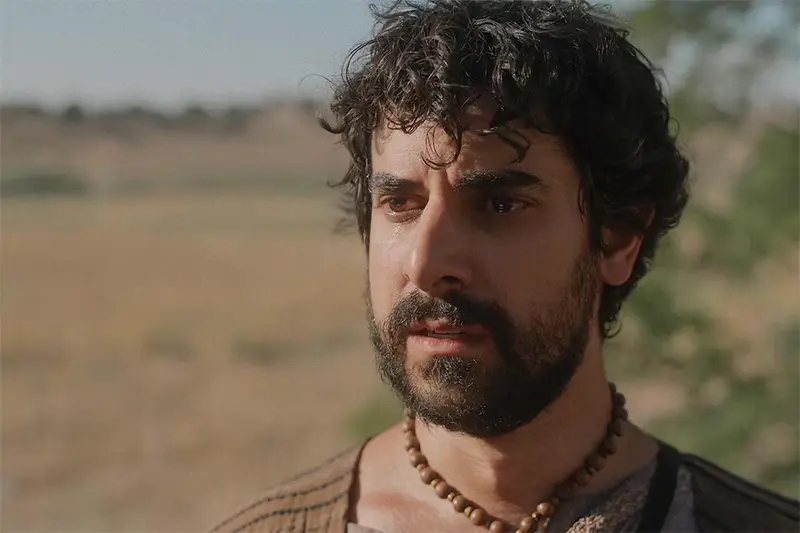 Retrato de un actor interpretando a Tomás apóstol, con una expresión de profunda reflexión o tristeza, y un collar de cuentas de madera.