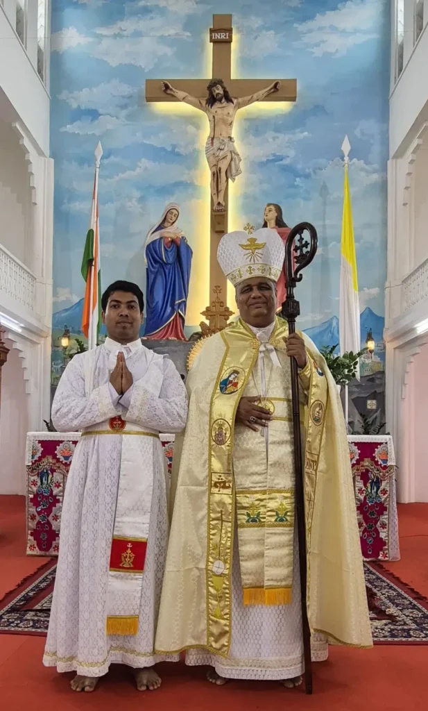 El recién ordenado diácono Melwin Thurakal posa junto al obispo consagrante frente al altar tras la misa de su ordenación diaconal.