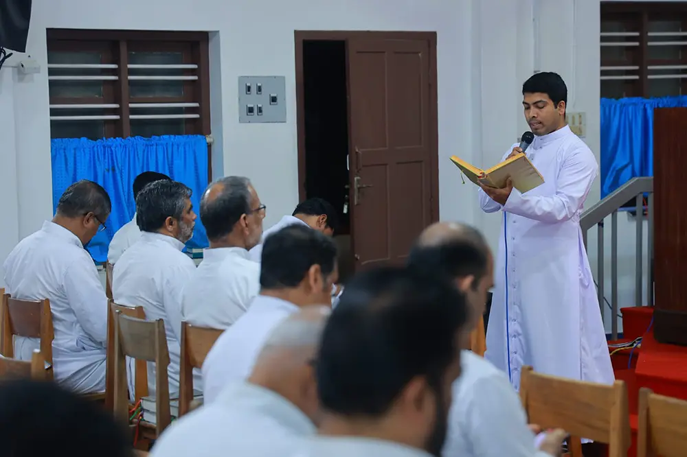 El diácono Melwin Thurakal proclamando la Palabra de Dios desde un libro ante la asamblea durante su ceremonia de ordenación diaconal.