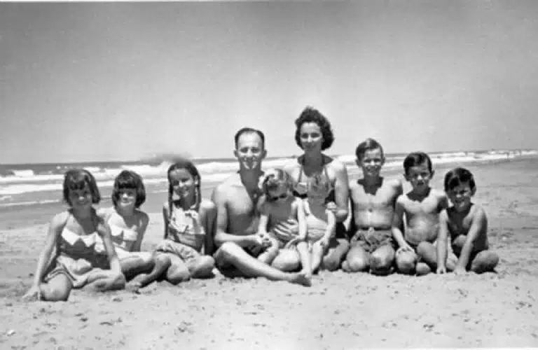 Fotografía en blanco y negro de Enrique Shaw y su familia sentados en la playa, sonriendo y mirando a cámara.